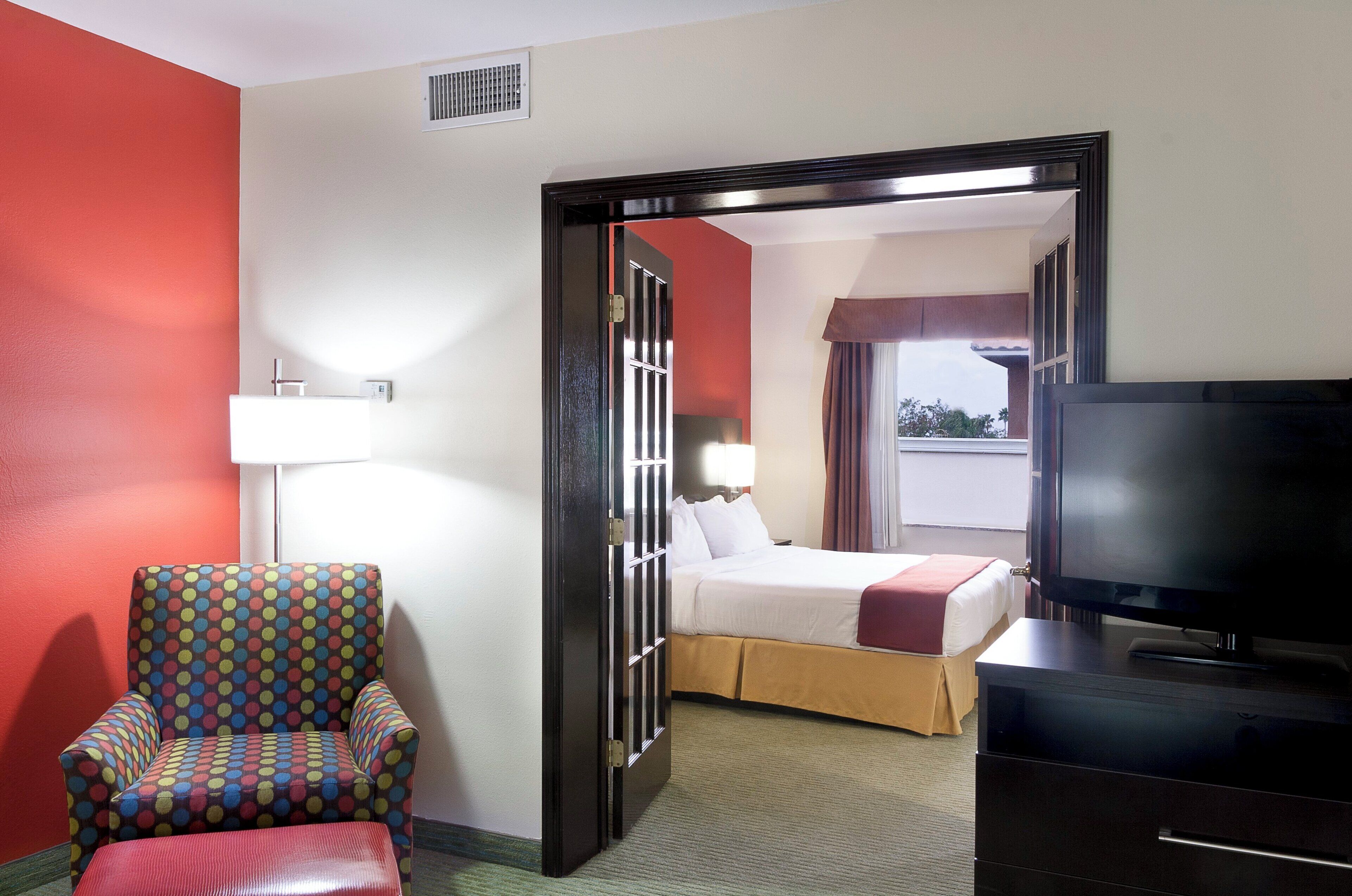 A hotel room with a bed, a TV, a chair, and a window with curtains.