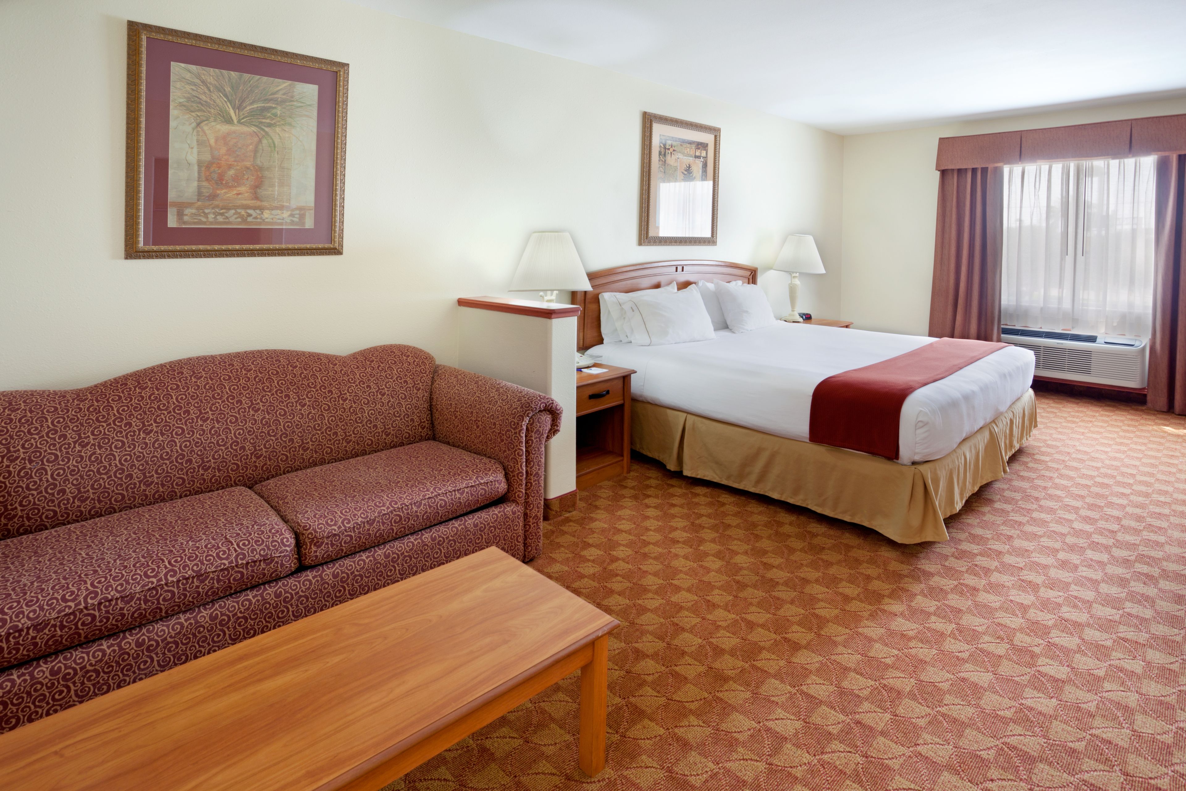 A hotel room with a bed, a sofa, a nightstand, two lamps, and a window with curtains.