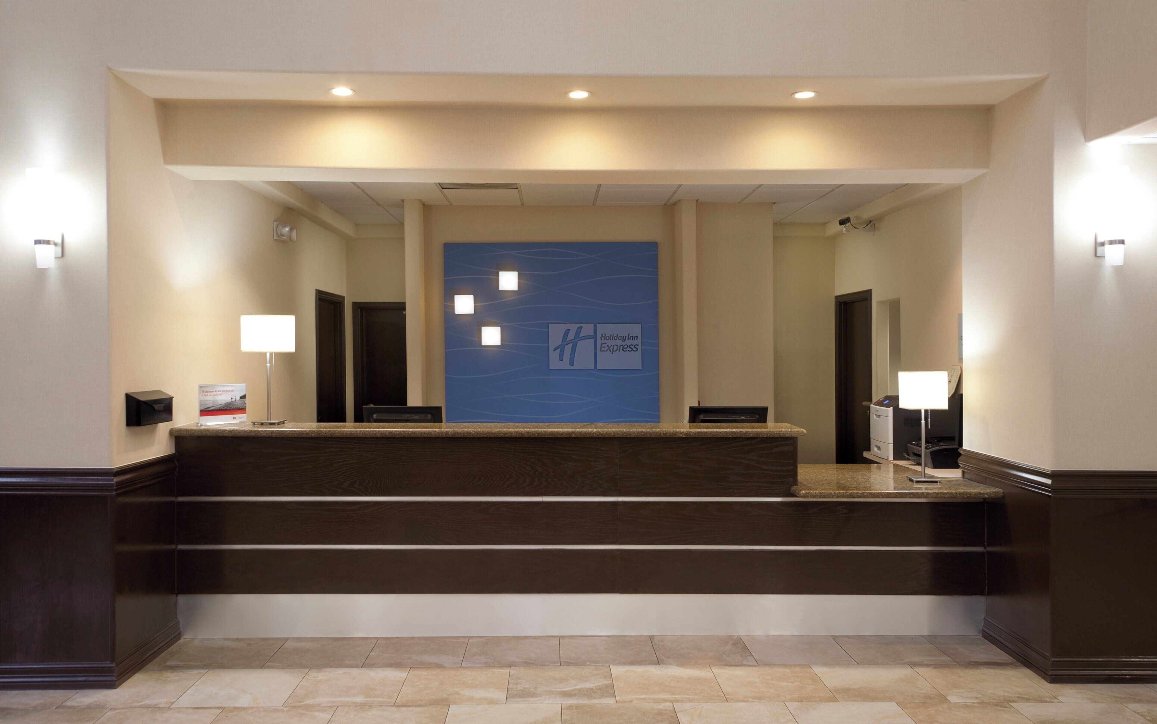 Un comptoir d’accueil avec un mur bleu orné du logo de Holiday Inn Express, un téléviseur à écran plat et une imprimante.