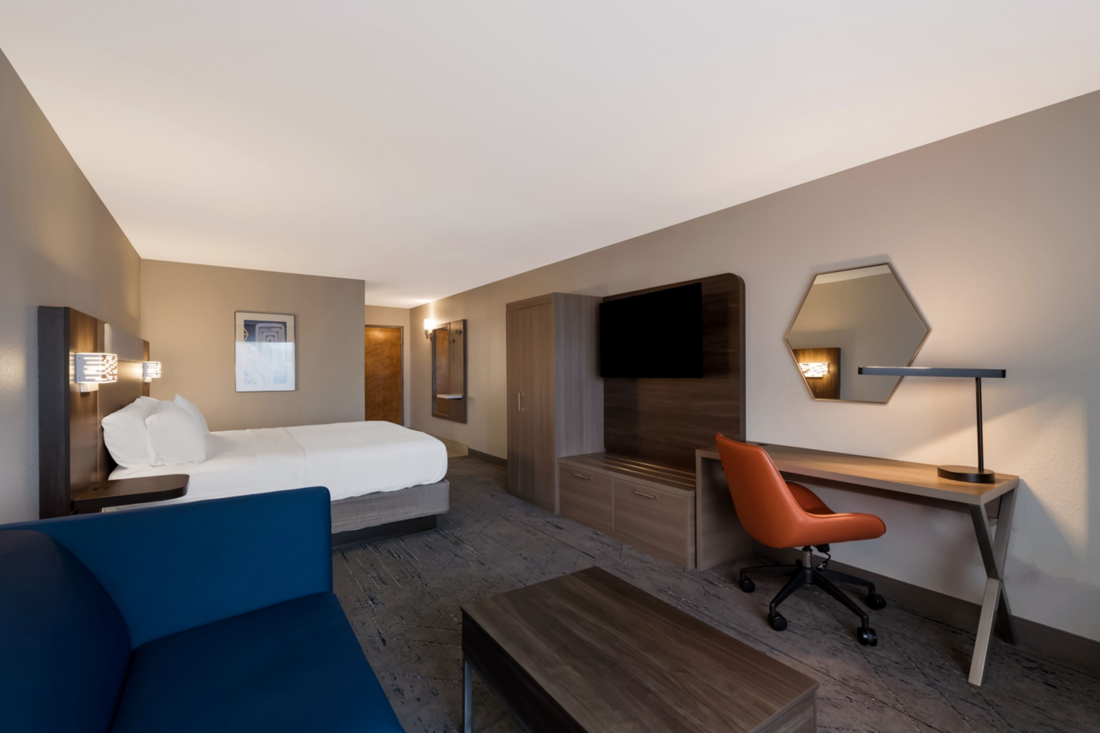 A modern hotel room with a bed, a desk, a chair, a sofa, and a TV.
