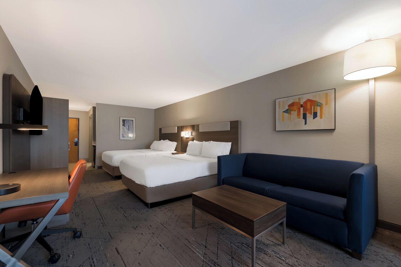 A hotel room with a bed, a desk, a chair, a sofa, a lamp, and a painting on the wall.