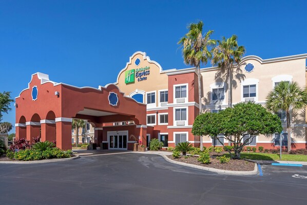 Um hotel com fachada vermelha, placa com 'Hilton Express Suites' e estacionamento com palmeiras.