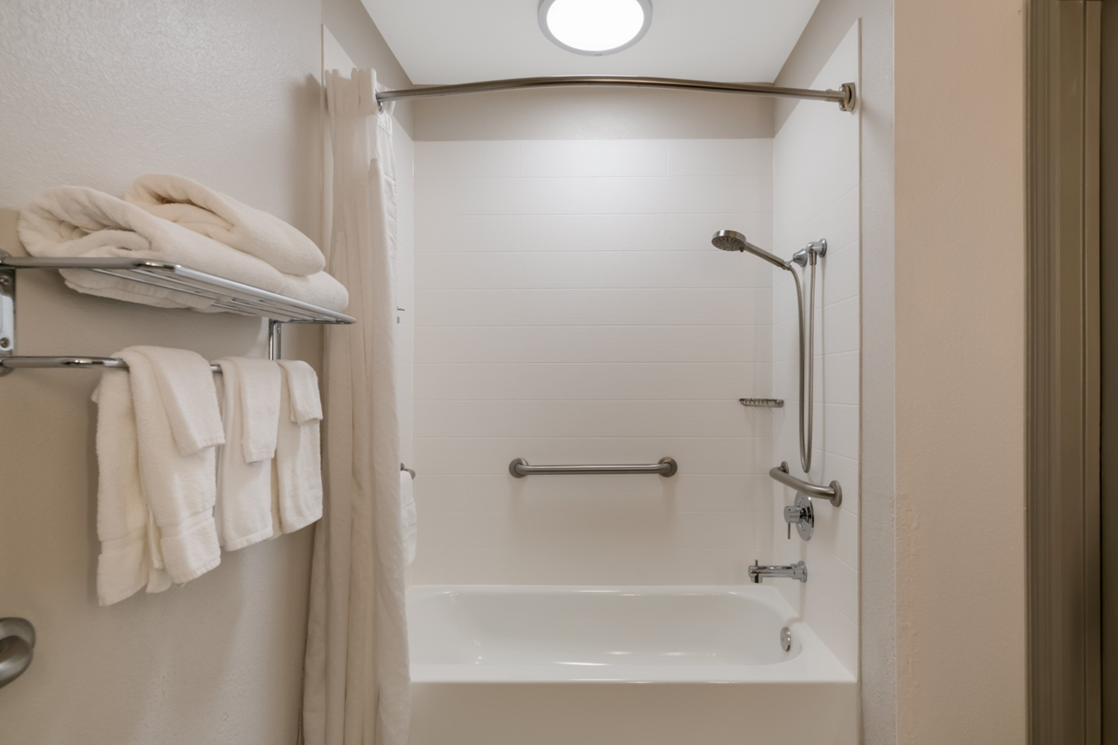 A modern bathroom with a bathtub, a shower with a handheld showerhead, and a towel rack with neatly folded towels.