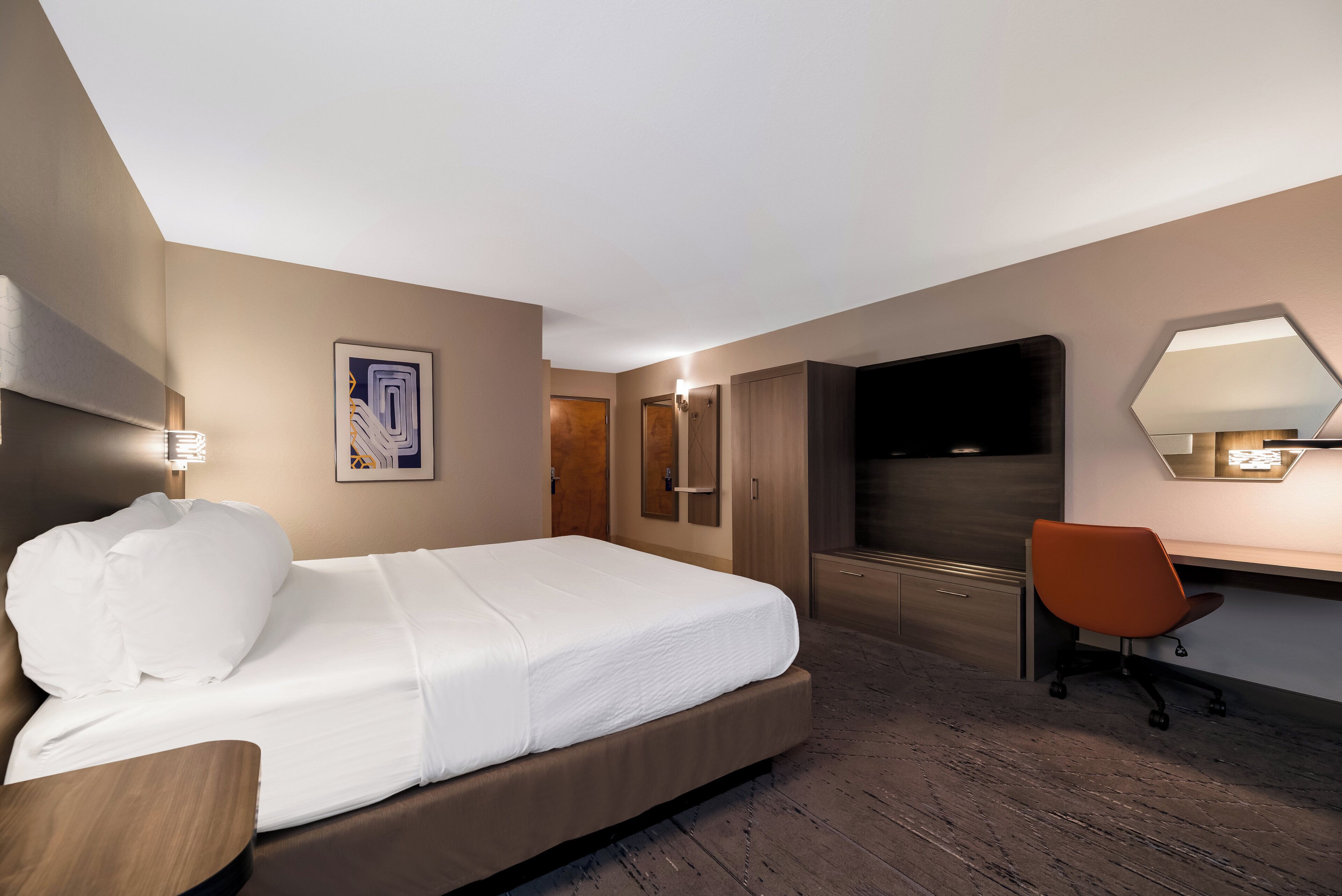A hotel room with a bed, a desk, a chair, a TV, and a mirror.