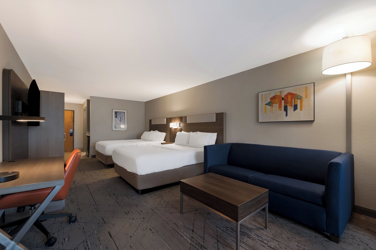 A hotel room with a bed, a desk, a chair, a sofa, and a lamp.