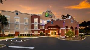A Holiday Inn Express & Suites with a classic architectural design, featuring a central entrance with a covered walkway, multiple windows, and a parking area with marked spaces. - Holiday Inn Express Hotel & Suites The Villages by IHG (Lady Lake)