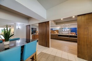 Cozinha moderna com armários de madeira, bancada e área de refeições com cadeiras azuis.