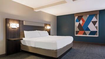 A modern hotel room with a large bed, wooden headboard, and a geometric wall art piece.