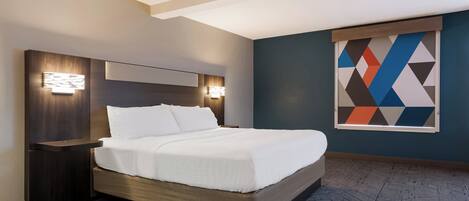 A modern hotel room with a large bed, wooden headboard, and a geometric wall art piece.
