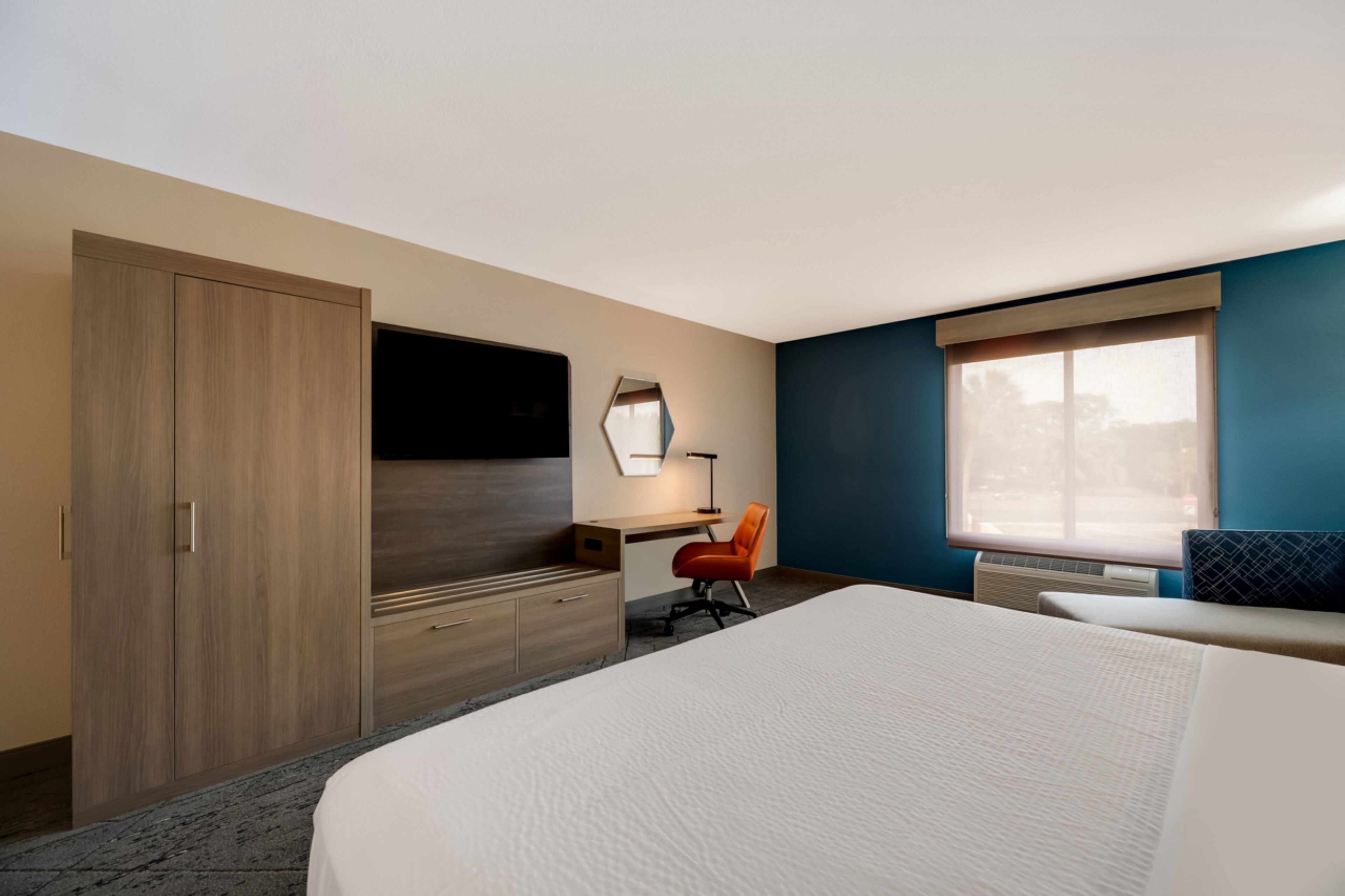A hotel room with a bed, a desk, a chair, a wardrobe, and a window.