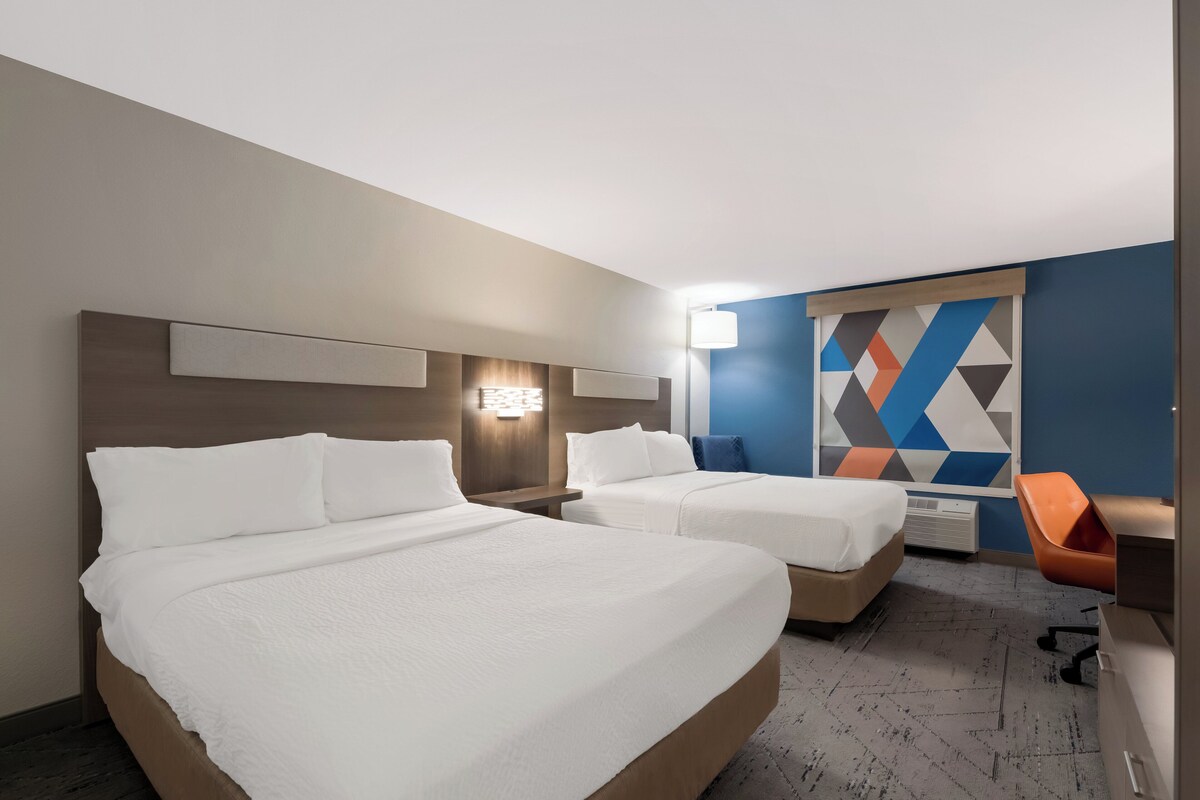 A hotel room with two beds, a desk, and a chair.