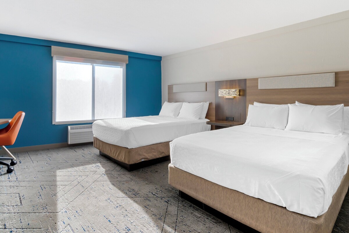 A hotel room with two beds, a desk, and a chair.