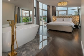 A modern bedroom with a large bed, a bathtub, and a view of the city.