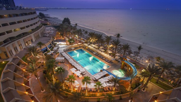 A resort with a swimming pool, beach, and palm trees. - Occidental Sharjah Grand (Sharjah)