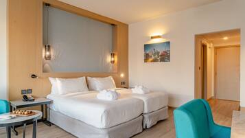 A hotel room with two beds, a small table with a phone and a plate of food, a painting on the wall, and a teal chair.