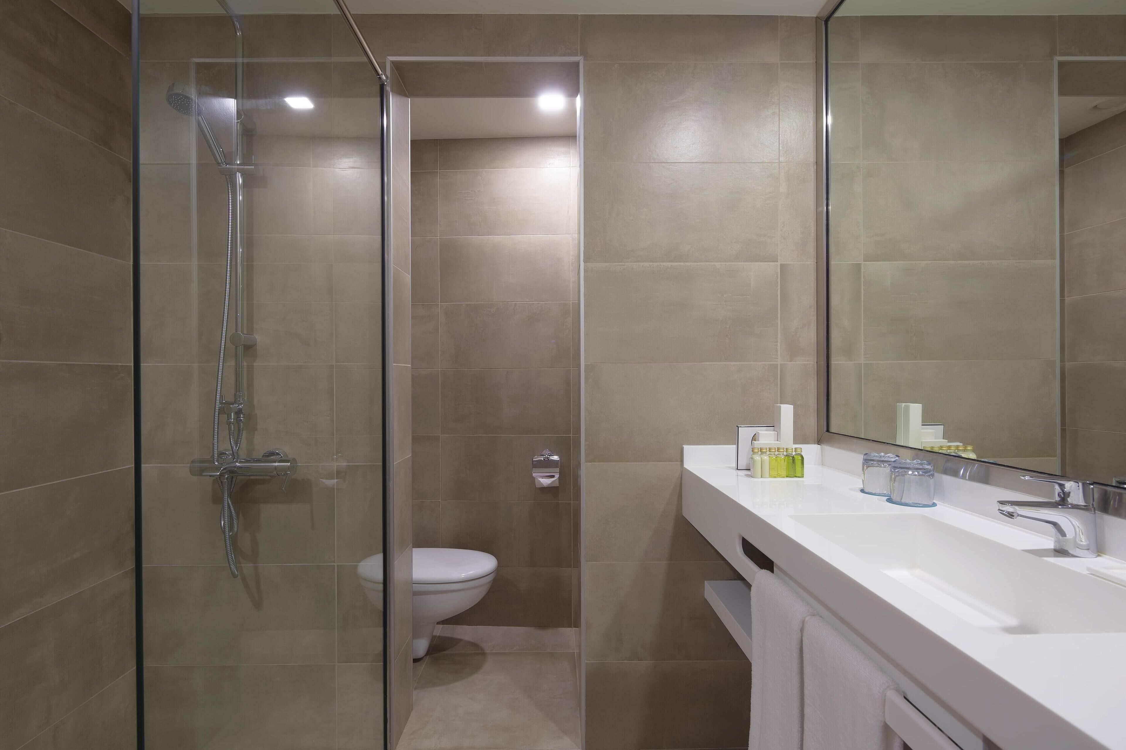 Un baño moderno con ducha de vidrio, inodoro y lavamanos blanco con espejo.