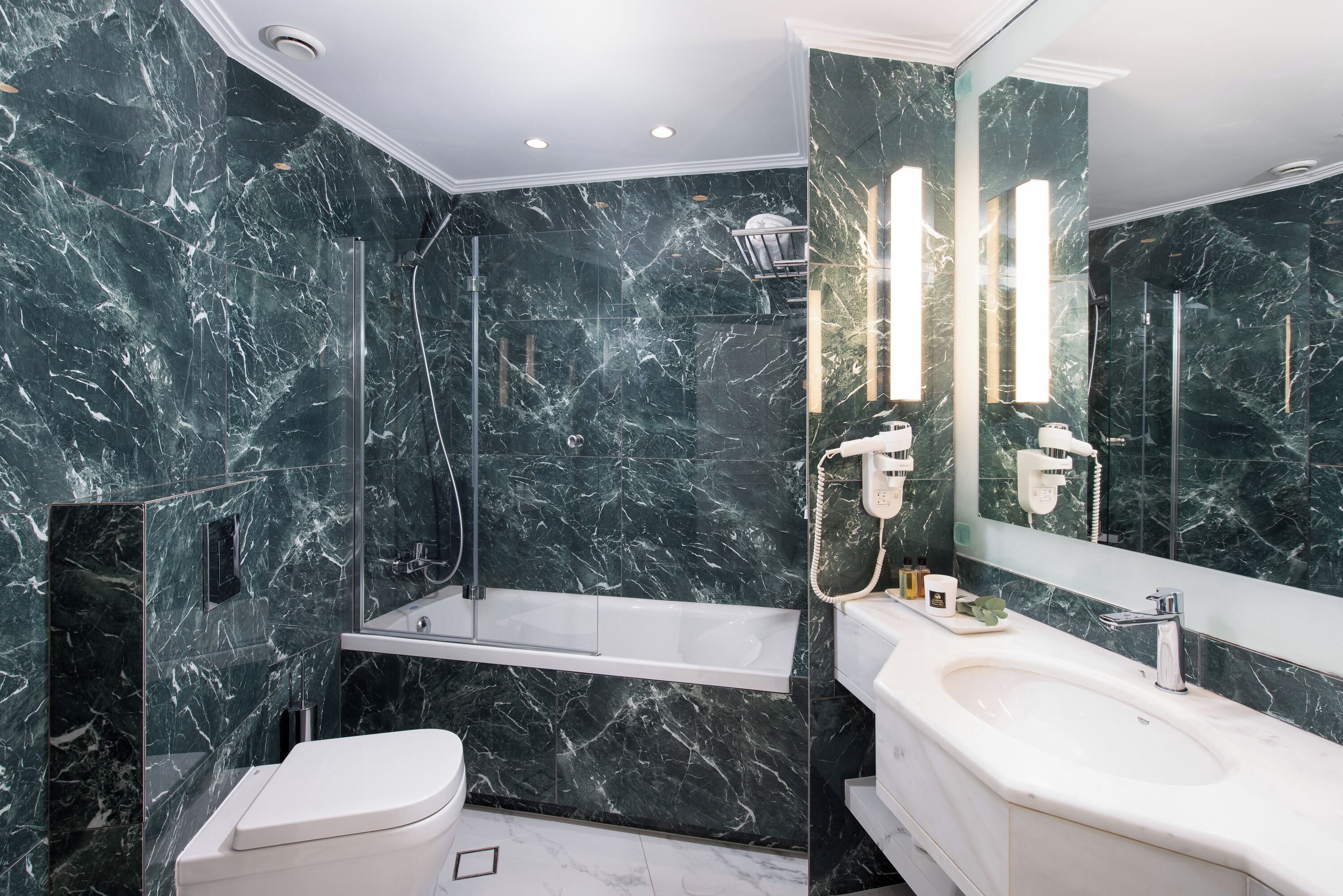 A modern bathroom with a marble wall, a bathtub, a toilet, and a sink with a mirror.