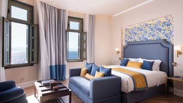 A bedroom with a bed, a sofa, a table, and a view of the sea through large windows.