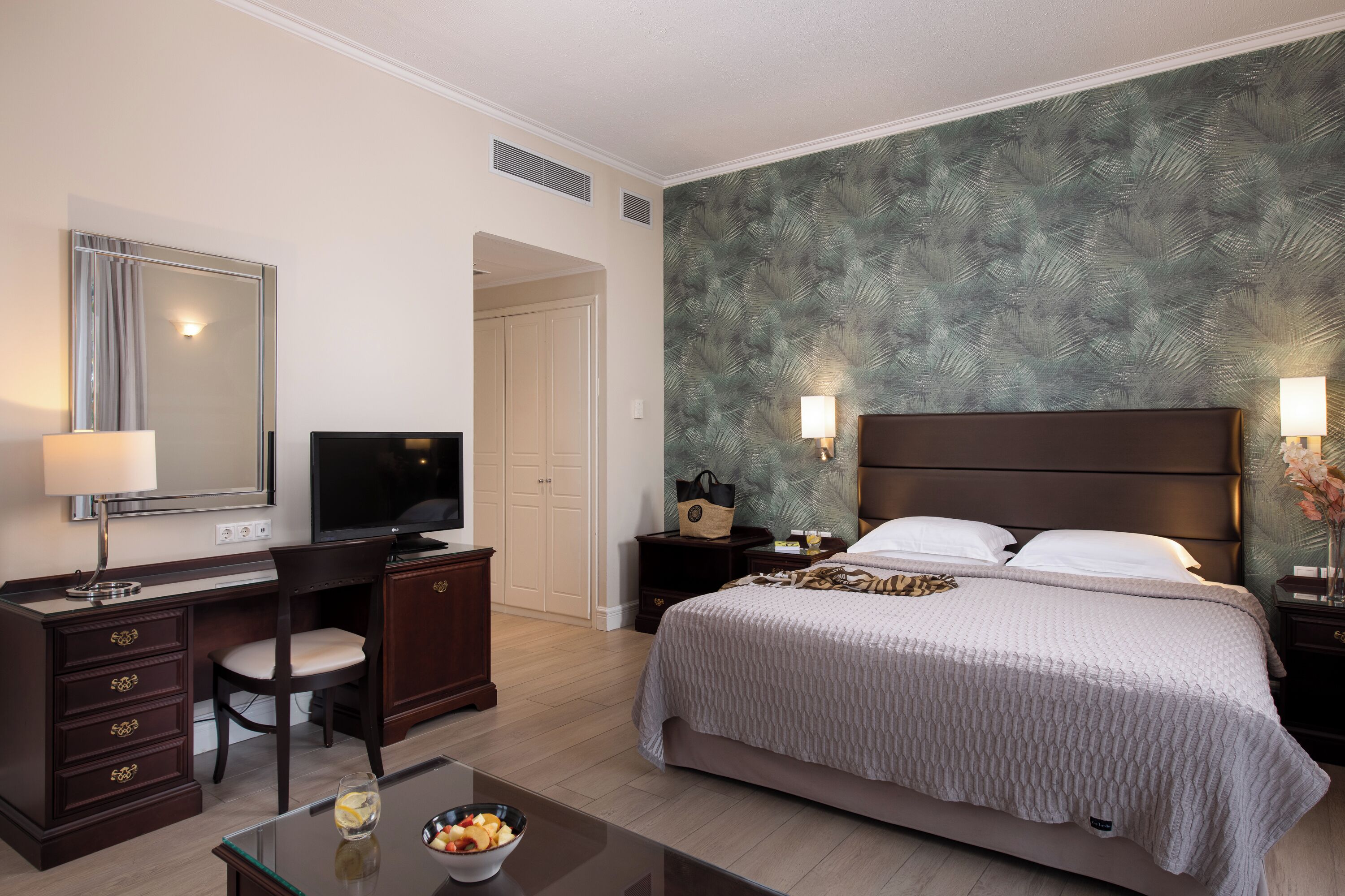 A hotel room with a bed, a desk, a chair, a television, and a nightstand with a lamp.