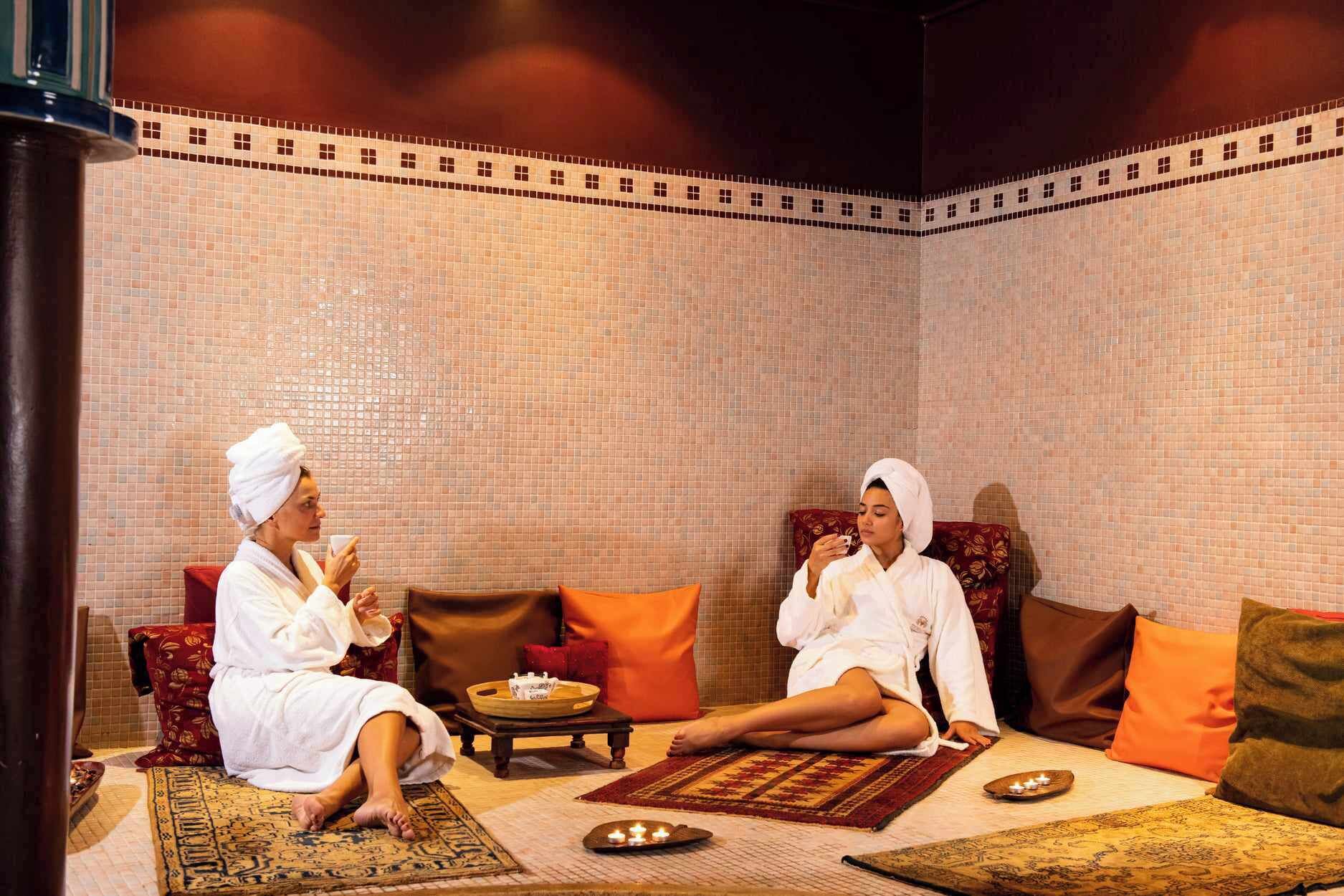 Una habitación con pared de azulejos, alfombra estampada y dos personas sentadas en un sofá.
