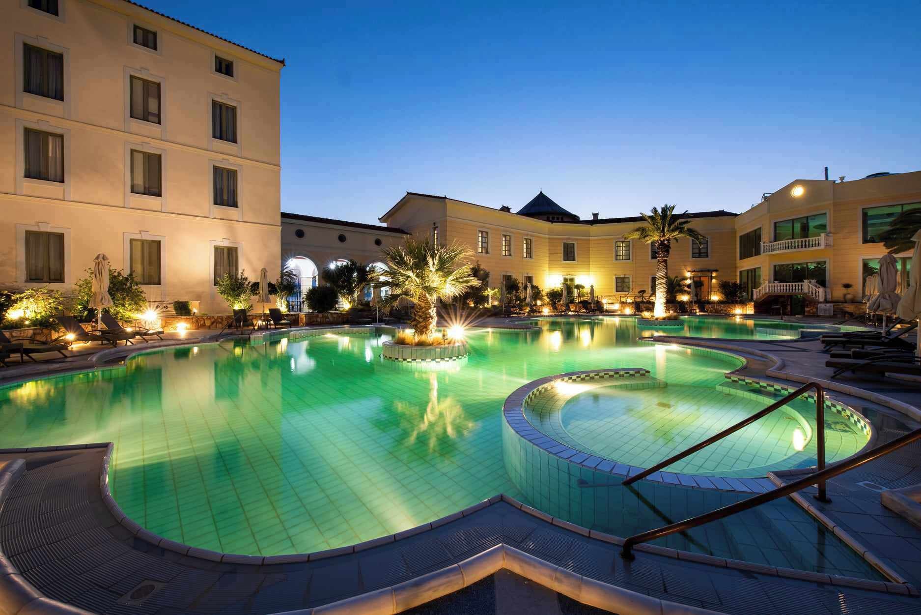 A hotel with a large outdoor swimming pool, multiple lounge areas, and a well-lit courtyard.