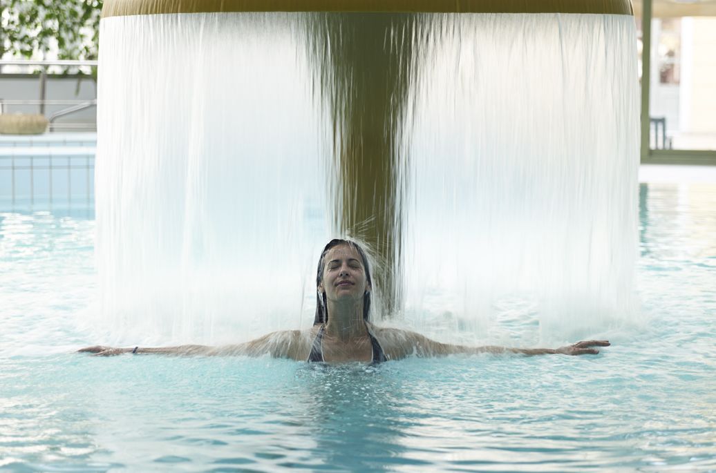 Eine Person im Schwimmbecken, über ihr befindet sich eine Wasserspielfeatur.