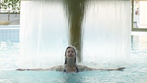A person in a swimming pool with a water feature above them.