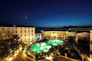 Un hotel con zona de piscina, varias edificaciones y vista al mar por la noche.