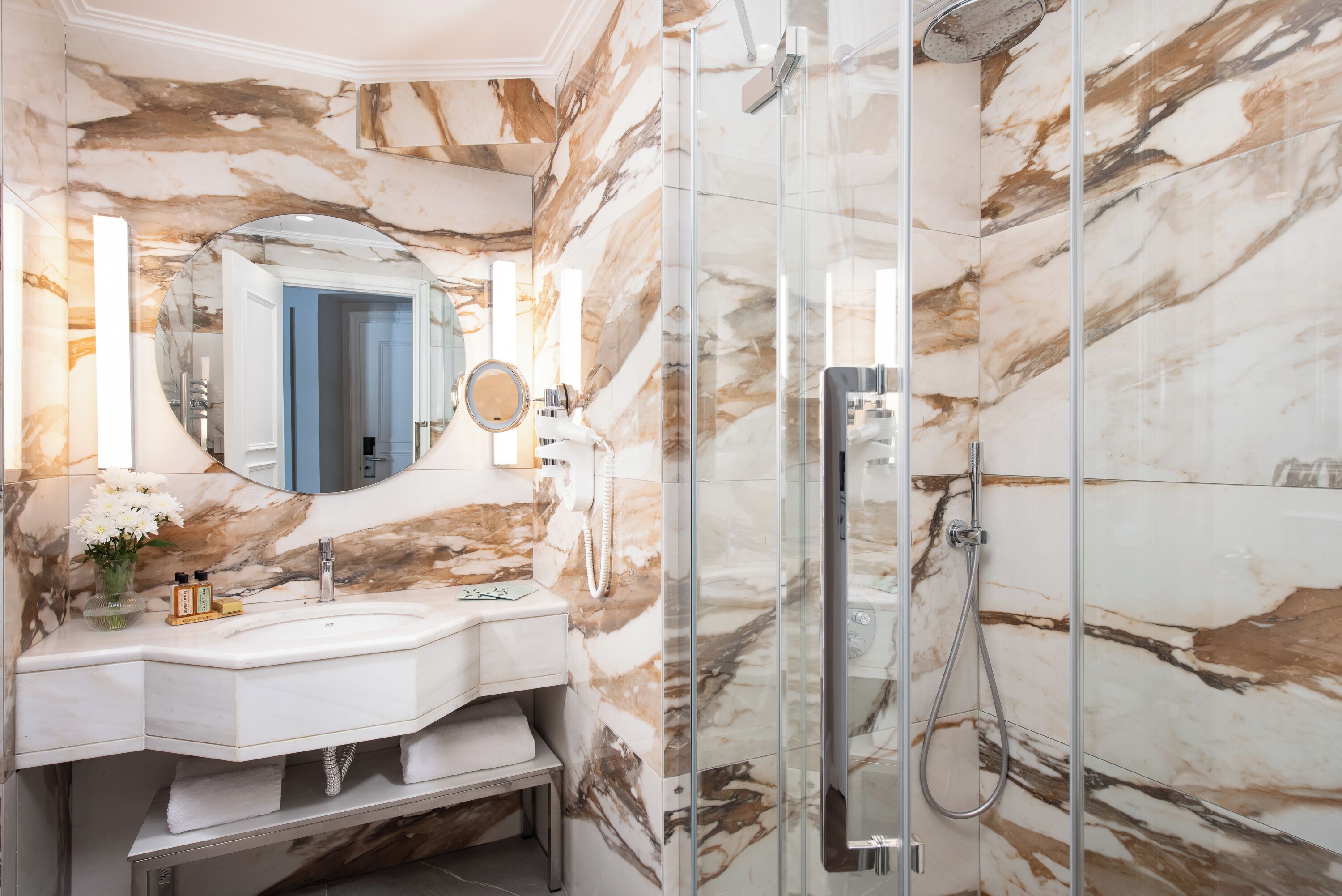 A bathroom with a marble wall, a glass shower enclosure, a sink, and a mirror.
