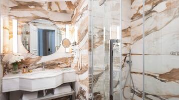 A bathroom with a marble wall, a glass shower enclosure, a sink, and a mirror.