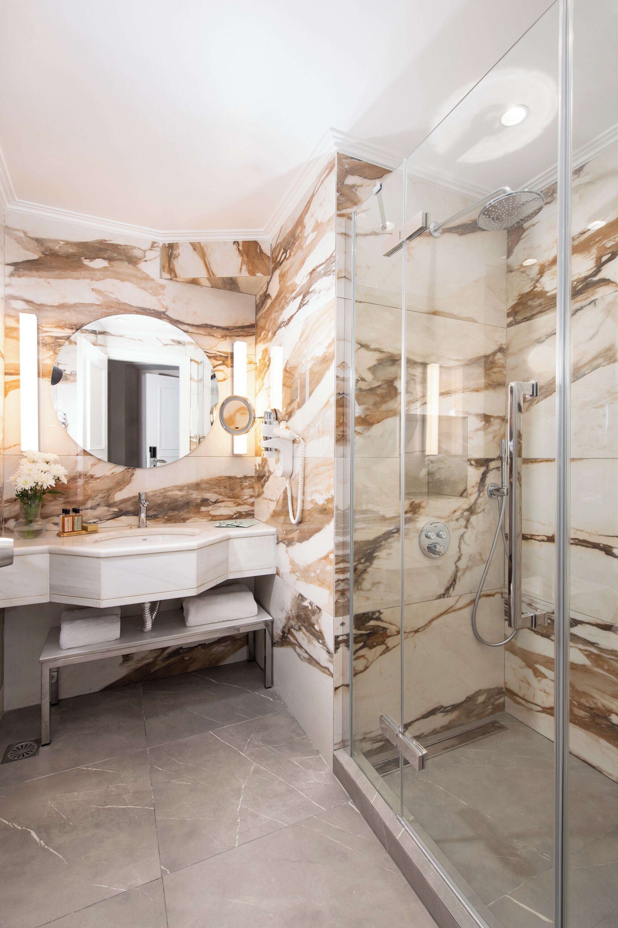 A bathroom with a marble wall, a glass-enclosed shower, and a vanity with a mirror.
