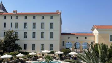 Une cour d’hôtel avec une piscine, des chaises longues, des parasols et des palmiers.