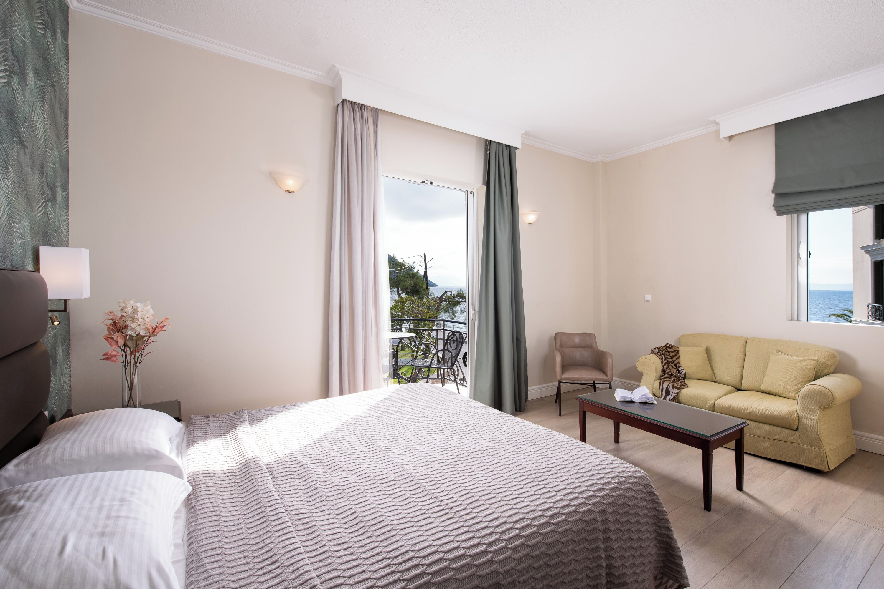 A hotel room with a bed, a sofa, a table, and a view of the outdoors.