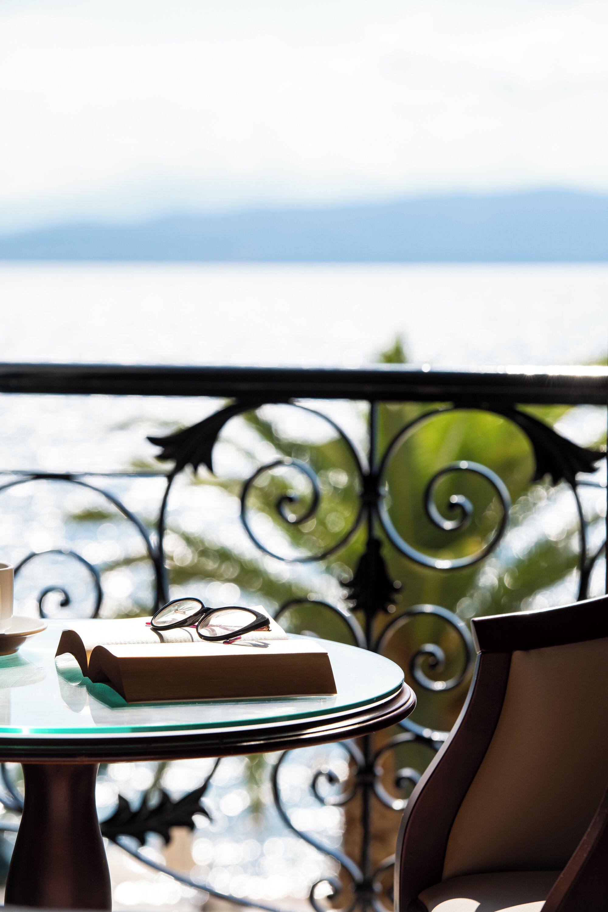 Mesa com um prato, copos e um livro, apoiada numa grades metálica com vista para o mar.