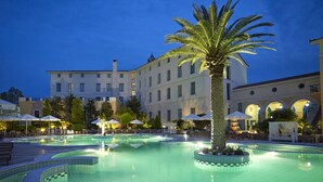 Un área de piscina con una palmera, sillas de descanso y sombrillas.