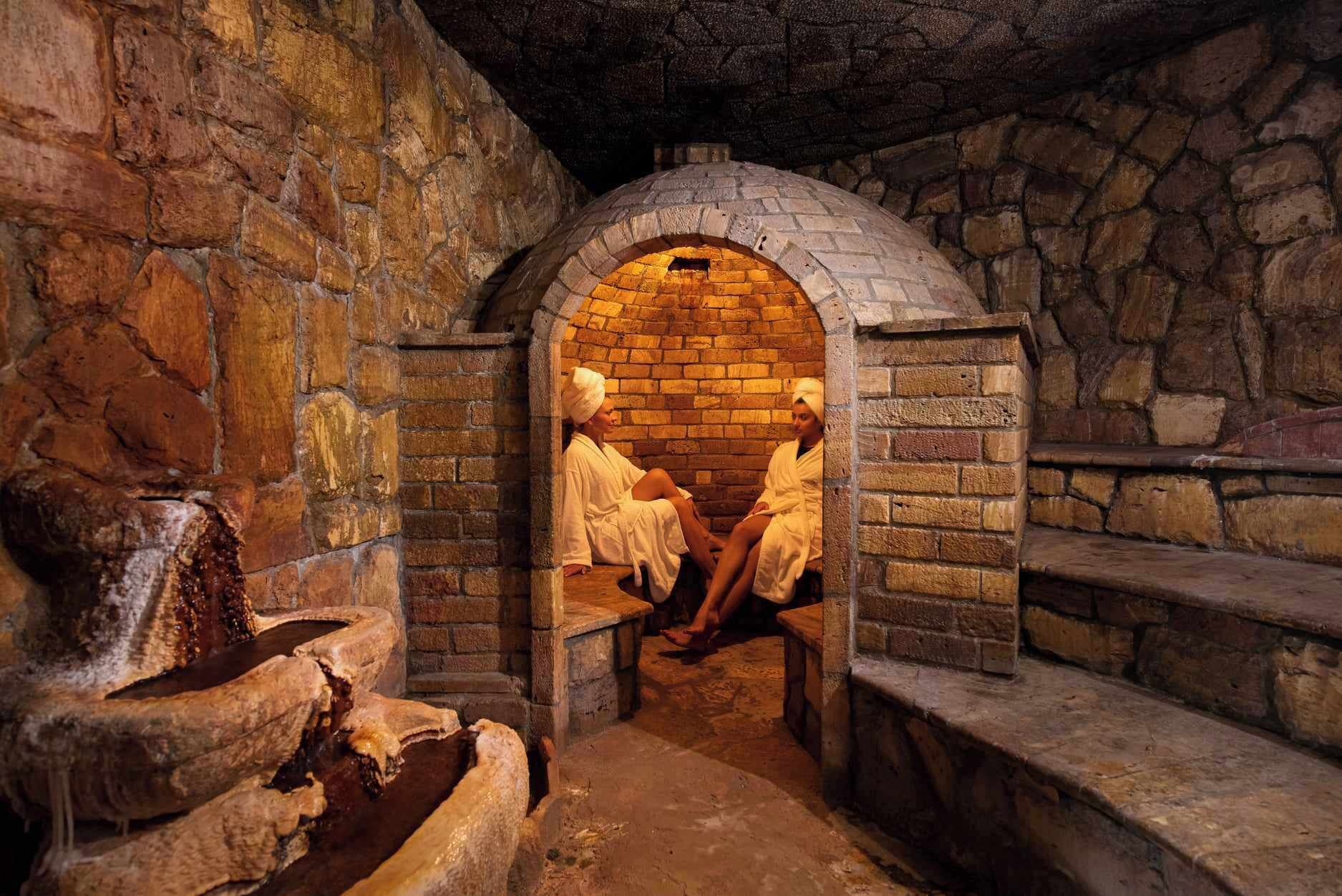 A stone-walled room with a brick oven, benches, and a water feature.