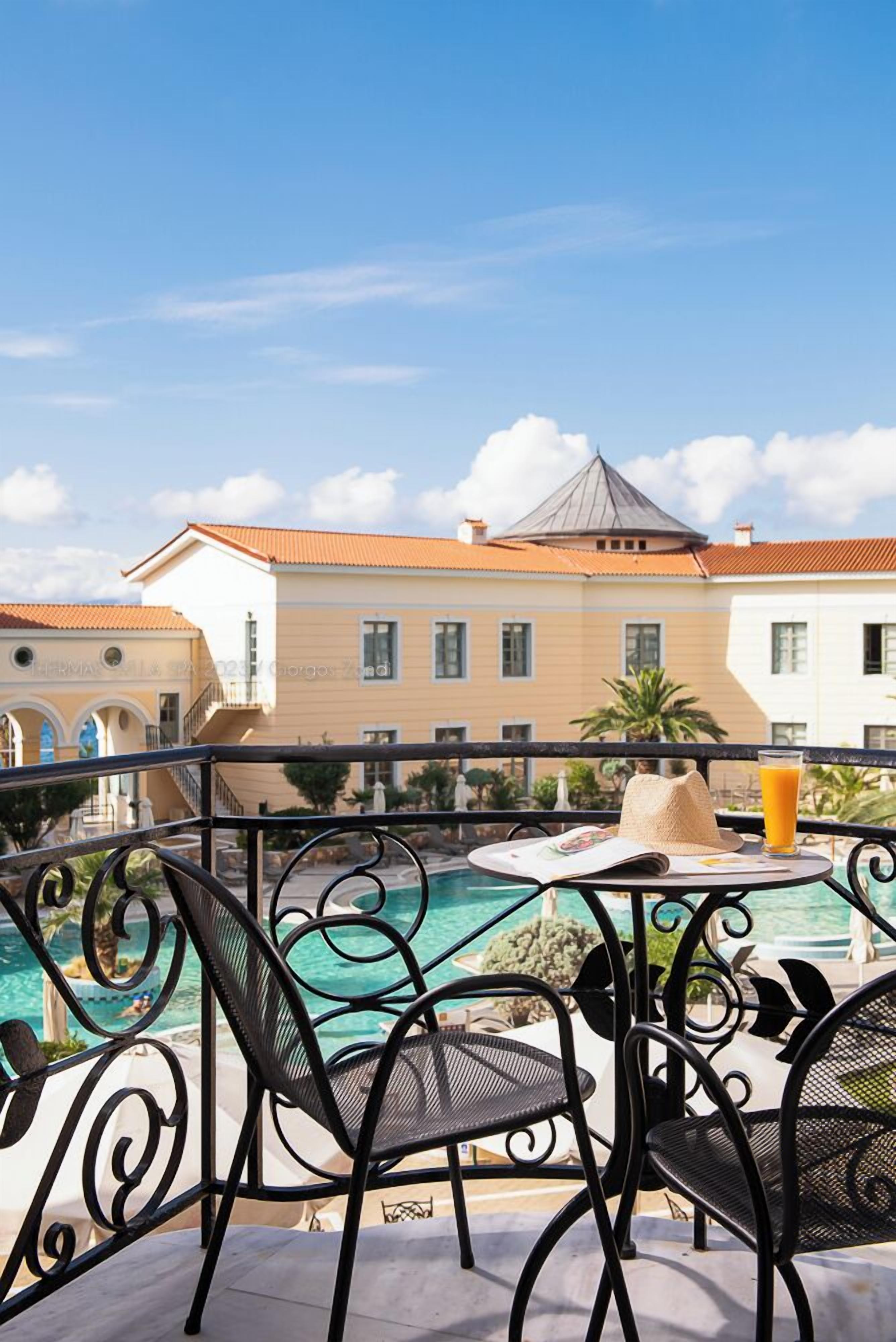 A poolside area with outdoor seating, a clear view of a building with a tiled roof, and a clear blue sky.