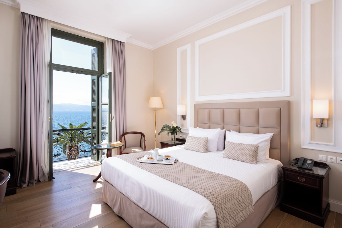 A hotel room with a large bed, a desk, a chair, and a view of the sea.
