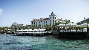 Un hotel frente al mar con un gran edificio, un muelle con sombrillas y palmeras.