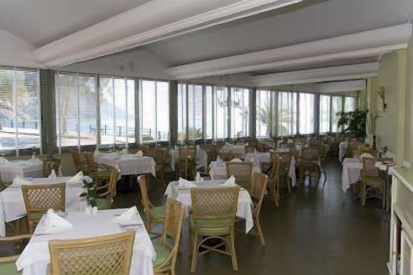 Un restaurant doté de nombreuses tables et chaises, de grandes fenêtres et offrant une vue sur l’extérieur.