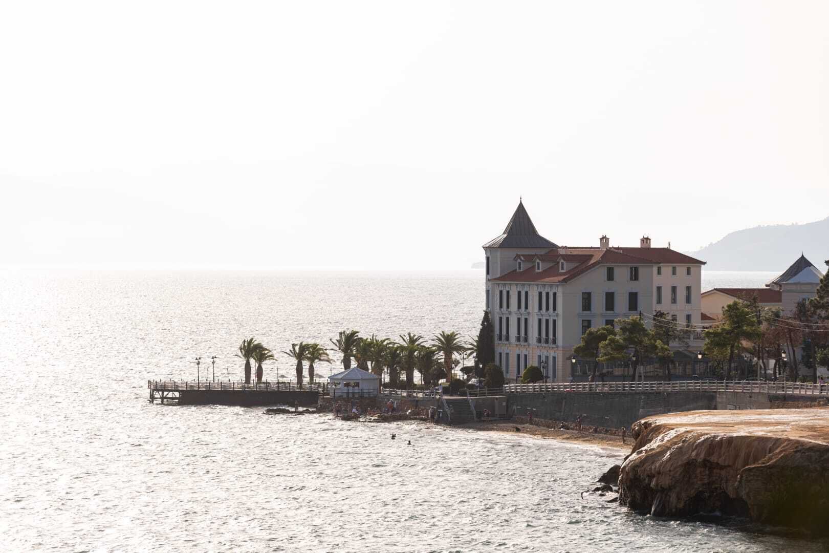 A coastal building with a tower, a pier, and palm trees.
