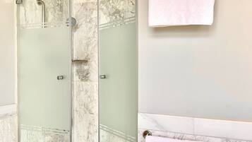 Une douche fermée par des parois de verre, avec un sol en marbre, un porte-serviettes sur lequel est posée une serviette blanche, et un mur en marbre.