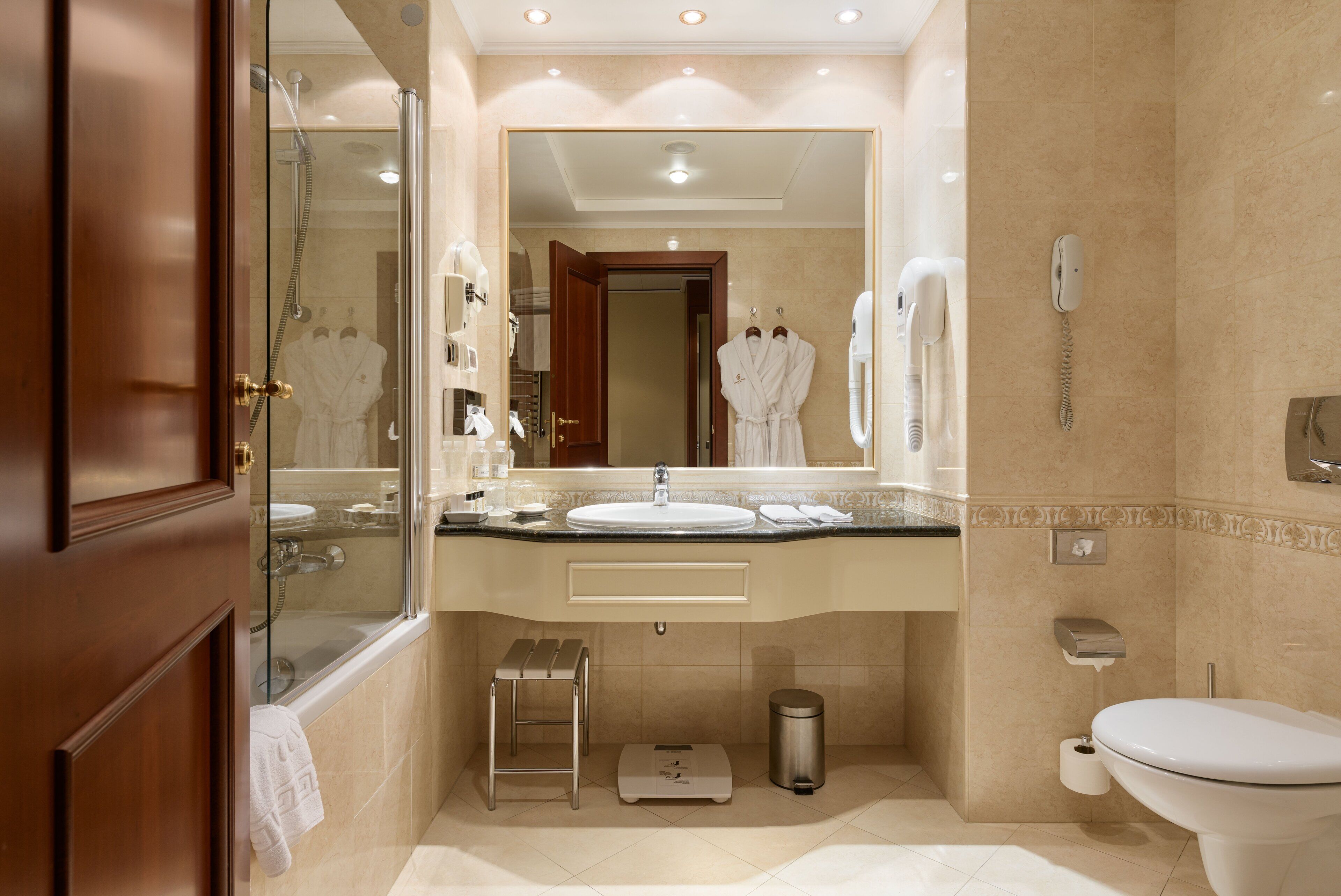 A modern bathroom with a glass-enclosed shower, a large mirror, a sink, a toilet, and a trash can.