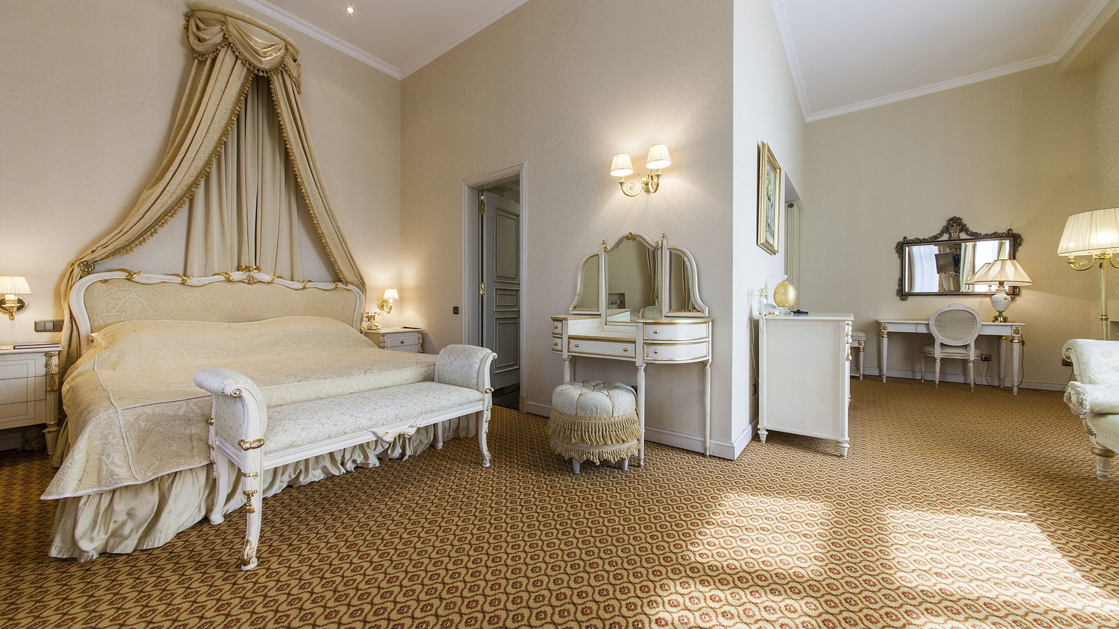 A spacious bedroom with a four-poster bed, a vanity with a mirror, a desk, and a chair.
