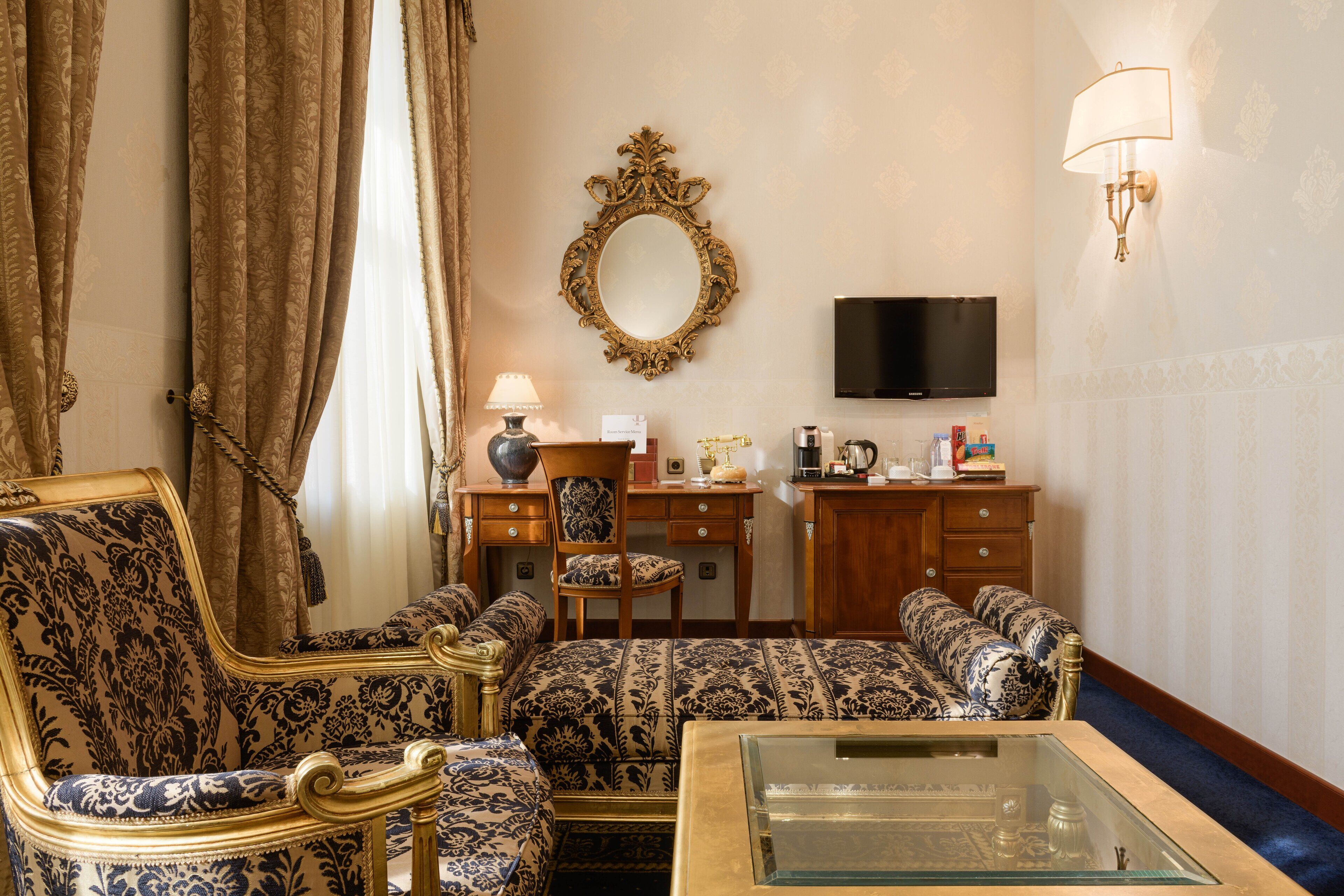 A room with a sofa set, a glass coffee table, a television, a desk with a chair, and a mirror on the wall.