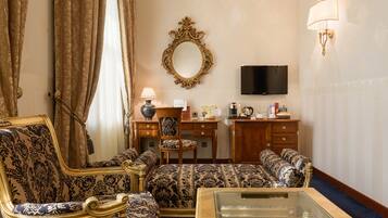 Una habitación con sofá, una mesa de centro de vidrio, televisor, escritorio con silla y espejo en la pared.