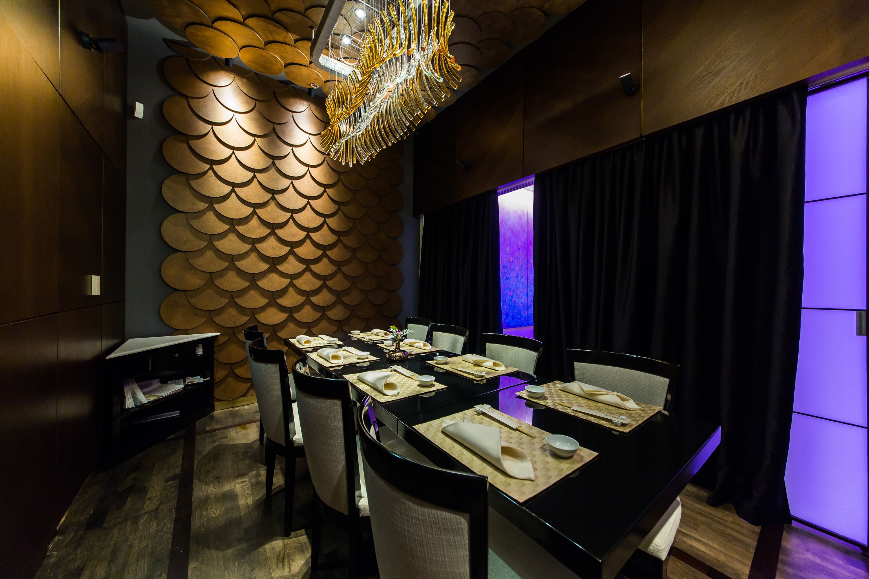 A dining area with a modern chandelier, a wall with a unique scalloped pattern, and a table set for six.