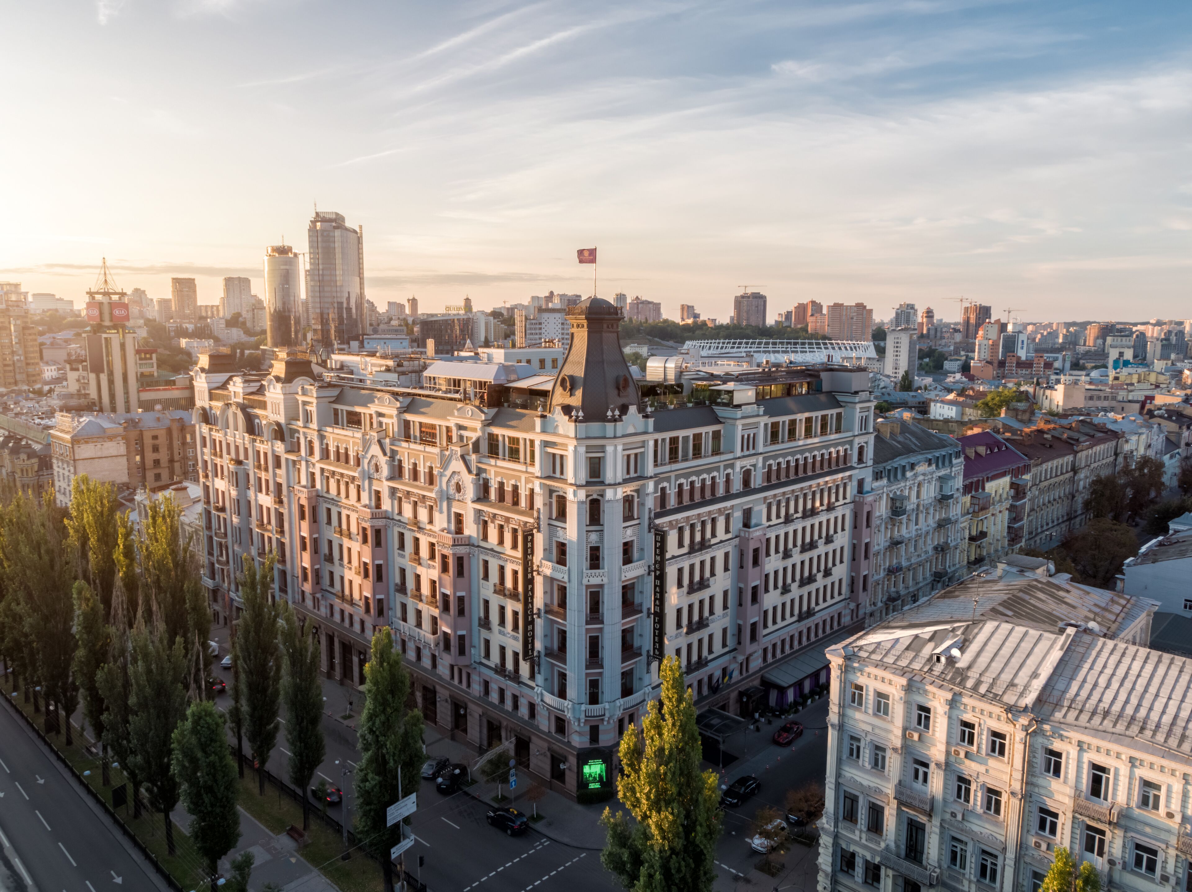 Un edificio grande e histórico con varios pisos y una torre destacada, rodeado de otros edificios y árboles.