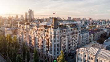 Un edificio grande e histórico con varios pisos y una torre destacada, rodeado de otros edificios y árboles.
