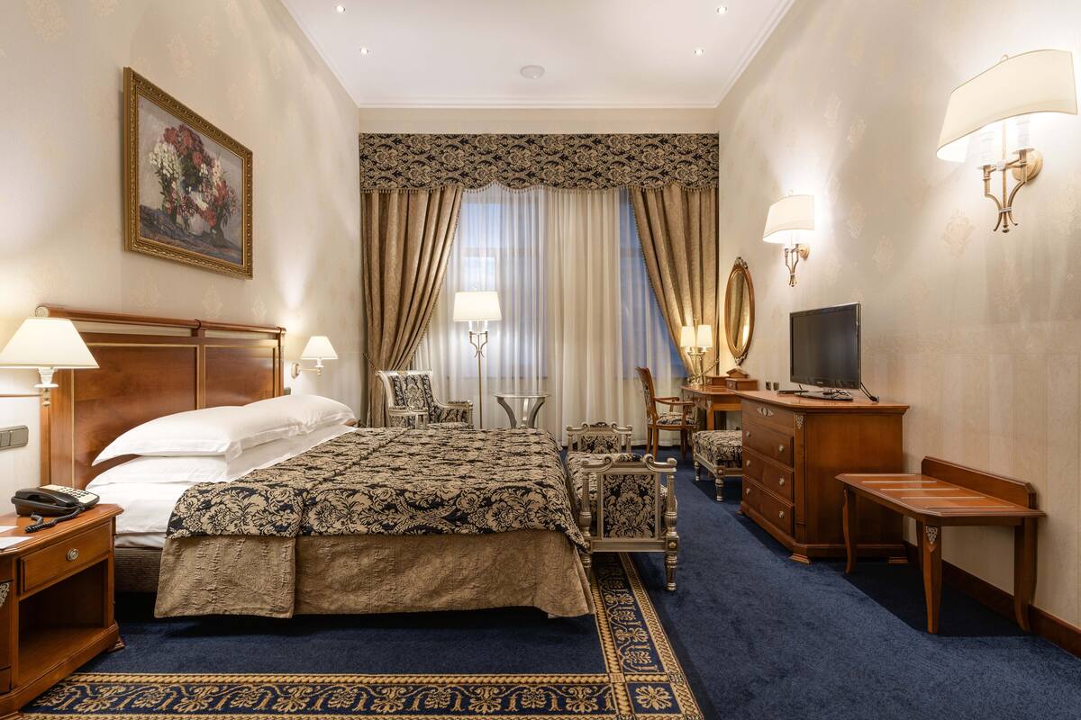 A hotel room with a large bed, a desk with a lamp, a television, and a dresser.